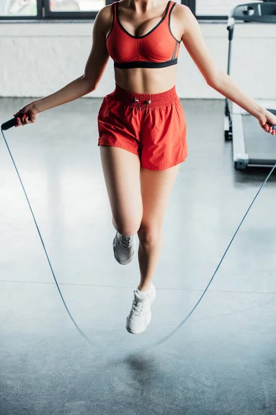Cropped view of sportive girl jumping while holding skipping rope in gym — Stock Photo