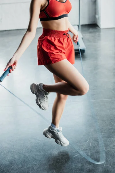 Cropped view of sportswoman jumping while holding skipping rope in gym — Stock Photo