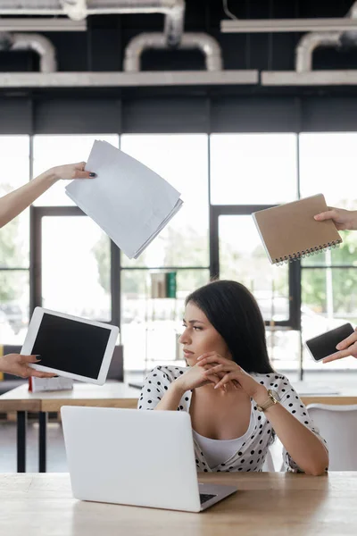 Businesswoman sitting near coworkers holding gadgets with blank screen, notebook and papers — Stock Photo