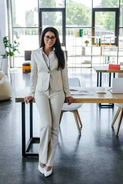 Donna felice in occhiali in piedi vicino al tavolo in ufficio — Foto stock