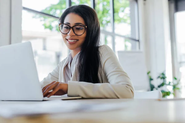 Selective focus of smiling businesswoman in glasses using laptop — Stock Photo