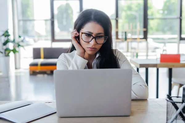 Upset businesswoman in glasses using laptop near notebook on table — Stock Photo