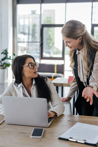 Selective focus of beautiful businesswoman looking at attractive coworker in glasses near gadgets on table — Stock Photo