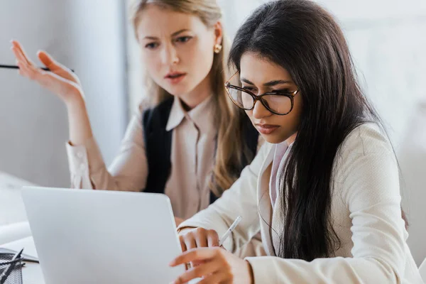 Enfoque selectivo de la mujer de negocios en gafas mirando portátil cerca de compañero de trabajo - foto de stock