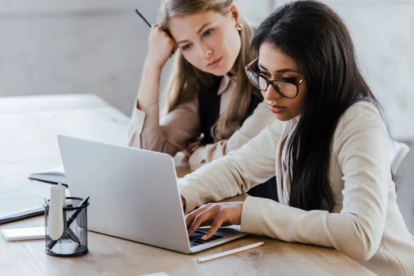 Selective focus of bored businesswomen looking at laptop in office — Stock Photo