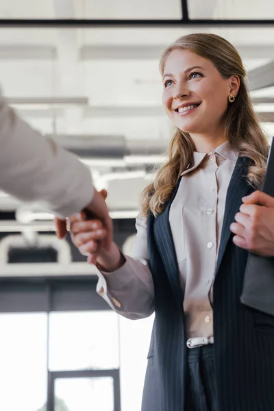 Enfoque selectivo de la alegre empresaria estrechando la mano con su compañero de trabajo en la oficina - foto de stock