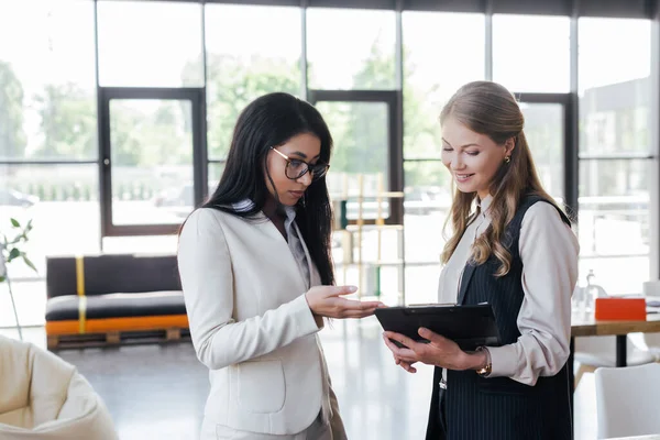 Businesswoman in glasses pointing with hand at clipboard near coworker in office — Stock Photo