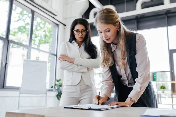 Enfoque selectivo de hermosa mujer de negocios firma contrato cerca de la mujer con los brazos cruzados — Stock Photo