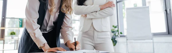 Concepto horizontal de empresaria firmando contrato cerca de compañero de trabajo con brazos cruzados - foto de stock