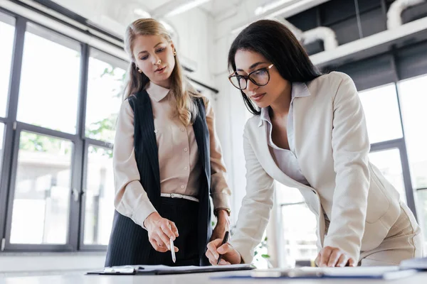 Selective focus of attractive businesswoman in glasses signing contract near coworker with pen — Stock Photo