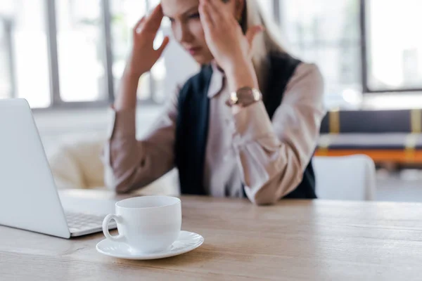 Foco seletivo de xícara com café perto de empresária exausta e laptop — Fotografia de Stock