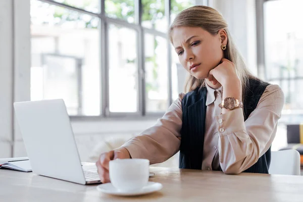 Selective focus of exhausted businesswoman touching cup of coffee near laptop — Stock Photo