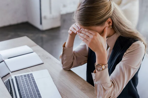 Donna d'affari che copre la faccia vicino a computer portatile e notebook in ufficio — Foto stock