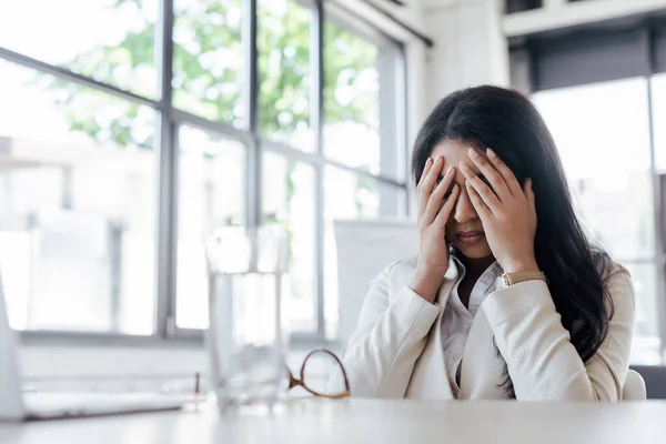 Fuoco selettivo di donna d'affari stanca che copre la faccia vicino a vetro d'acqua su tavolo — Foto stock