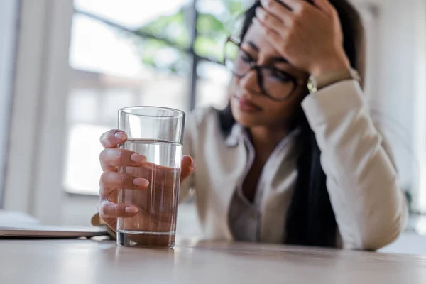 Selective focus of tired businesswoman holding glass of water in office — Stock Photo