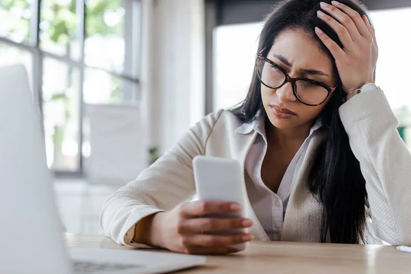 Foco seletivo de mulher de negócios triste usando smartphone perto do laptop — Fotografia de Stock