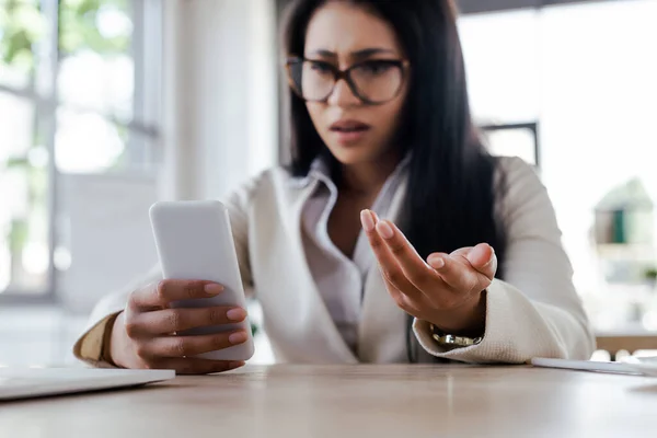 Вибірковий фокус незадоволеної бізнес-леді, використовуючи смартфон і жест в офісі — стокове фото