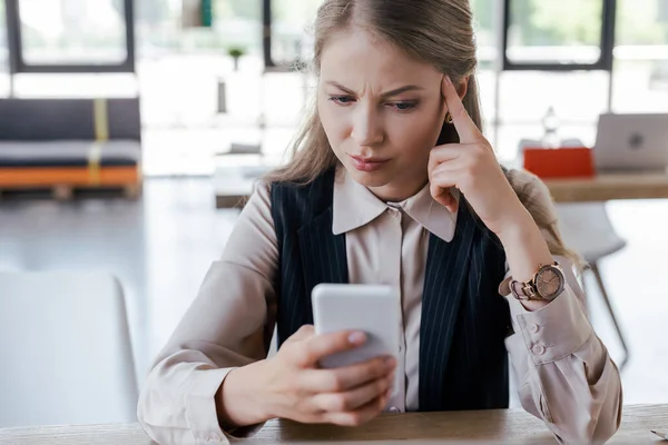 Selective focus of dissatisfied businesswoman using smartphone in office — Stock Photo