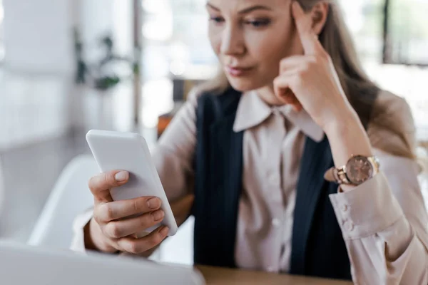 Selective focus of displeased businesswoman using smartphone in office — Stock Photo