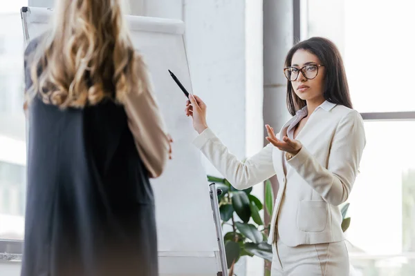 Foyer sélectif de la femme d'affaires dans les lunettes geste près de tableau à feuilles mobiles et en regardant collègue — Photo de stock