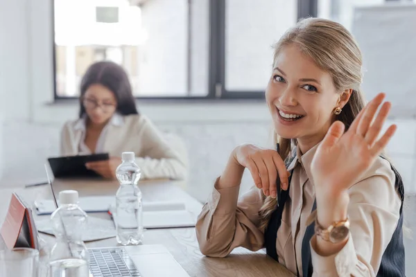 Selektiver Fokus einer glücklichen Geschäftsfrau, die im Amt mit der Hand winkt — Stockfoto