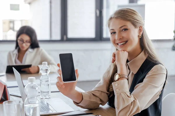 Selective focus of happy businesswoman holding smartphone with blank screen — Stock Photo