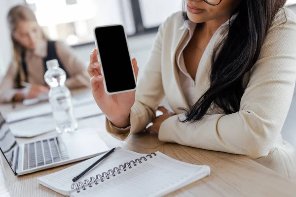 Vista recortada de la mujer de negocios sosteniendo teléfono inteligente con pantalla en blanco - foto de stock
