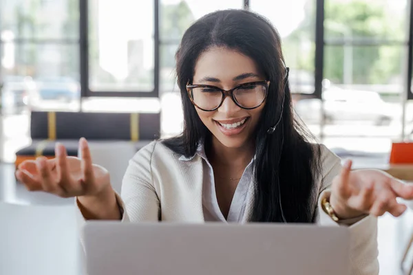 Selective focus of happy operator in headset gesturing while looking at laptop — Stock Photo