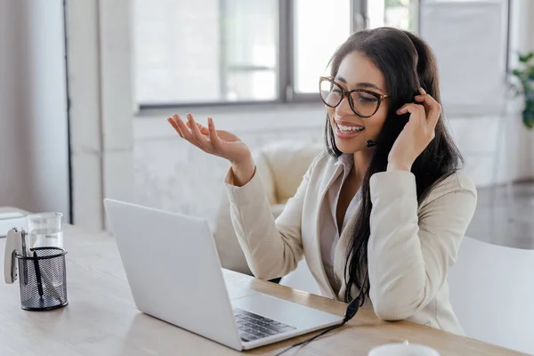 Operador feliz en el gesto de auriculares mientras mira el ordenador portátil - foto de stock