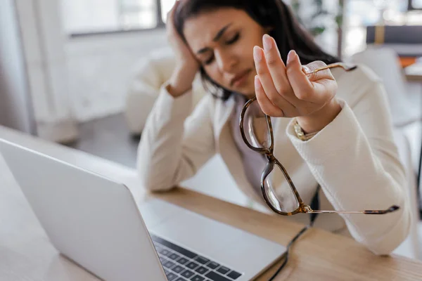 Fuoco selettivo di donna stanca che tiene occhiali vicino a computer portatile in ufficio — Foto stock