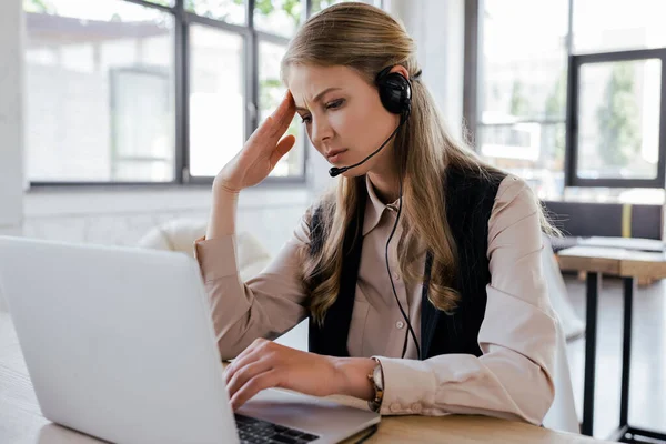 Selective focus of tired operator in headset looking at laptop — Stock Photo