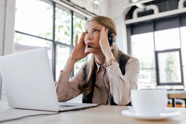 Selective focus of tired operator in headset looking up near cup and laptop — Stock Photo