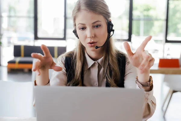 Selective focus of operator in headset gesturing while talking near laptop — Stock Photo