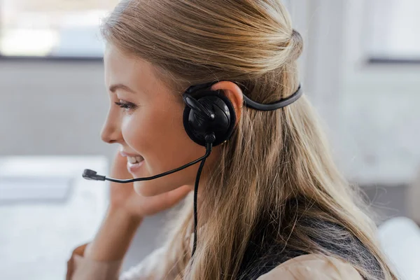 Side view of cheerful operator in headset smiling in office — Stock Photo