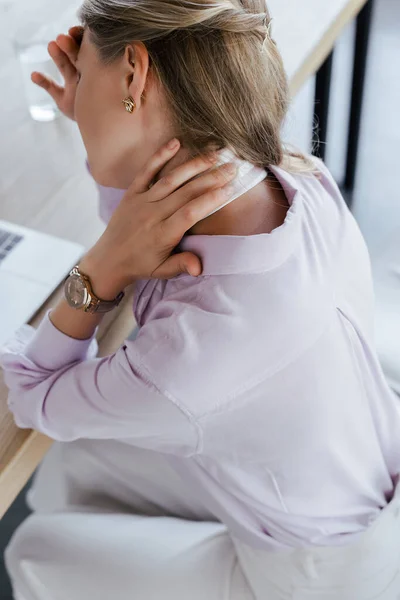 Selective focus of businesswoman feeling pain while touching neck in office — Stock Photo