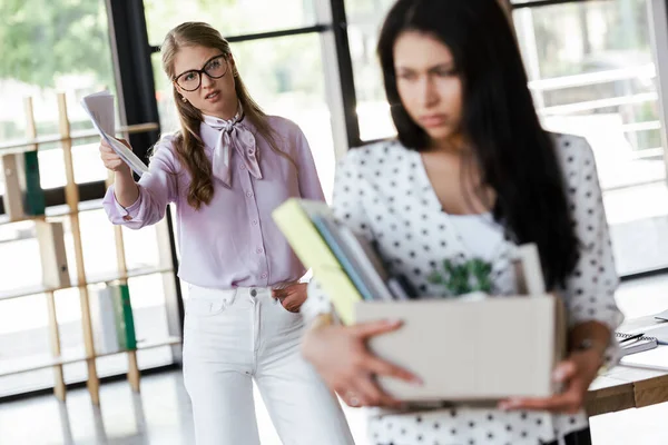 Foyer sélectif de patron mécontent debout avec la main dans la poche près du gestionnaire licencié tenant boîte avec des dossiers et des documents — Photo de stock