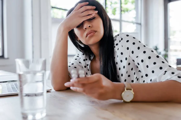 Selective focus of woman with headache holding pills near glass of water — Stock Photo