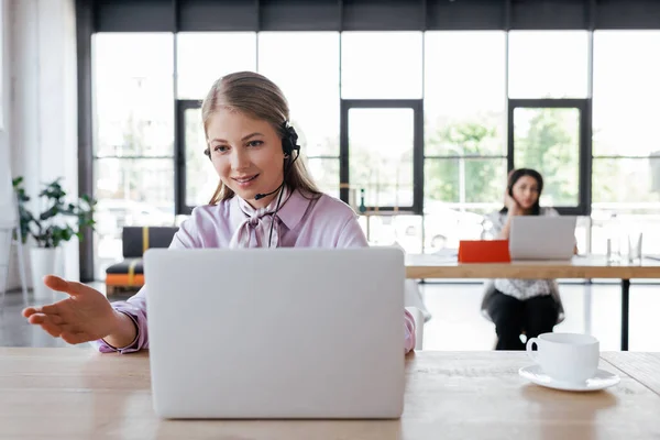 Selective focus of attractive operator in headset gesturing while looking at laptop near coworker — Stock Photo