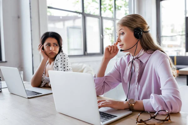 Selective focus of surprised operator touching headset near coworker in office — Stock Photo