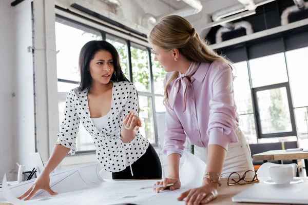 Selective focus of attractive businesswomen looking at each other near blueprints on table — Stock Photo