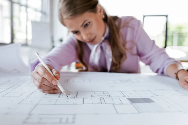 Selective focus of beautiful businesswoman drawing blueprints in office — Stock Photo