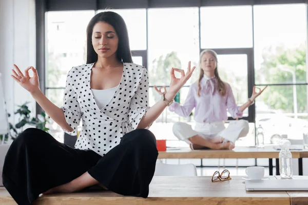 Selective focus of attractive businesswomen with closed eyes meditating in office — Stock Photo