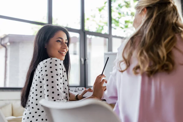 Enfoque selectivo de la mujer de negocios feliz sosteniendo lápiz y mirando a su compañero de trabajo - foto de stock