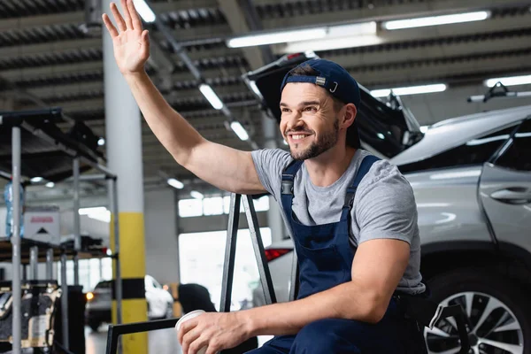 Glücklicher Mechaniker mit winkender Hand und Pappbecher in der Werkstatt — Stockfoto