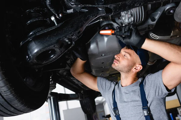 Gutaussehender Mechaniker hält Taschenlampe und repariert Auto in Tankstelle — Stockfoto