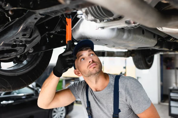 Schöner Mechaniker mit Taschenlampe und Blick auf Auto in der Tankstelle — Stockfoto