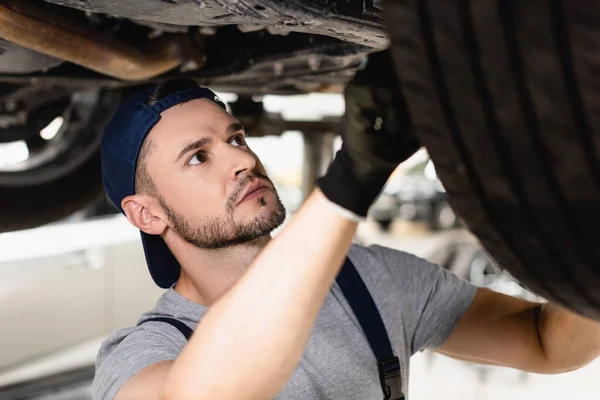 Selective focus of mechanic in rubber glove and cap fixing car — Stock Photo