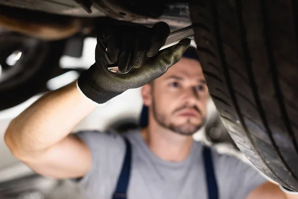 Selektiver Fokus des Mechanikers im Gummihandschuh, der Schraubenschlüssel hält und das Auto fixiert — Stockfoto