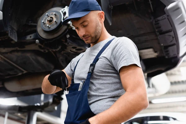 Tiefansicht des Mechanikers in Overalls, der Schraubenschlüssel aus Tasche in der Nähe des Autos nimmt — Stockfoto