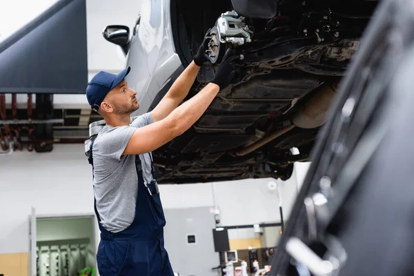 Selective focus of handsome mechanic in overalls repairing car — Stock Photo